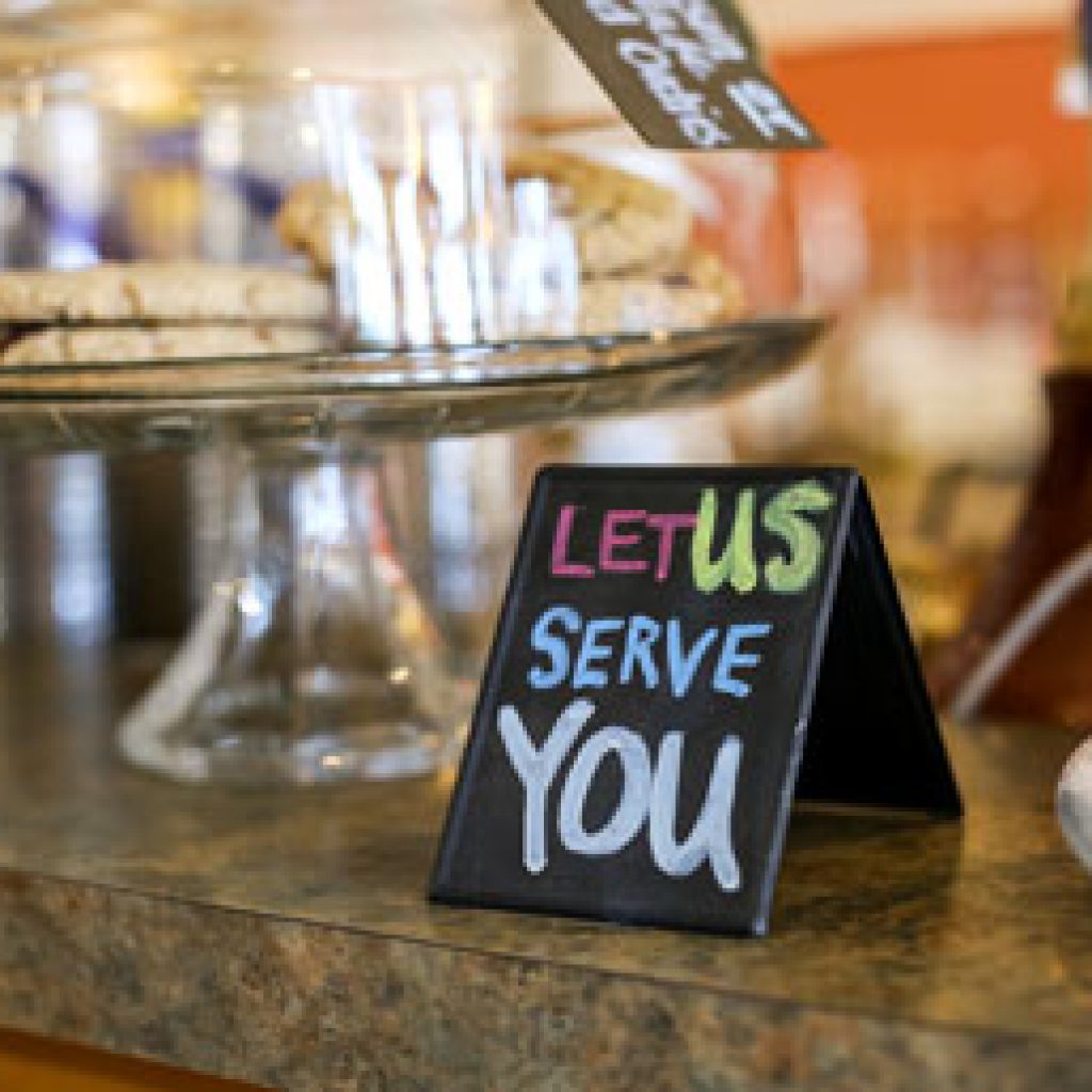 Let Us Serve You card in front of a dessert tray.