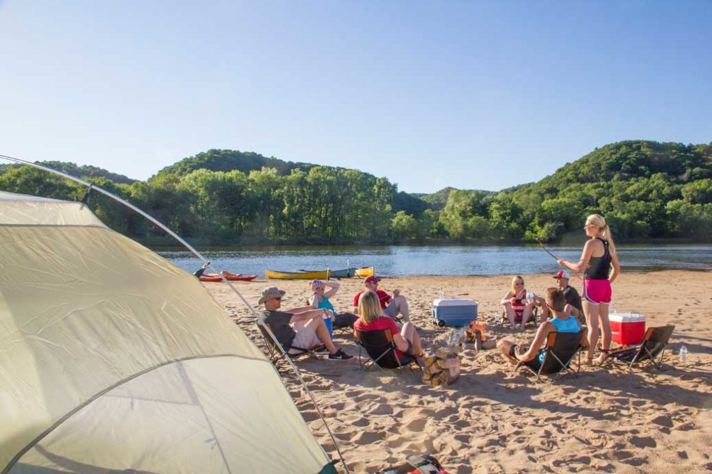 A group of people camping on the beach in front of a campfire.